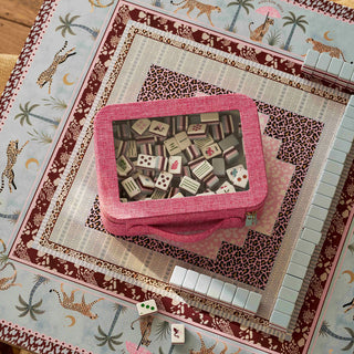 A pink fabric game box with a clear window showing mahjong tiles inside, placed on a decorative safari-themed game board with matching white tiles arranged around it.