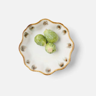 A small scalloped ceramic dish with a gold-toned rim and raised decorative details around the edge, holding three green Brussels sprouts on a light gray background.