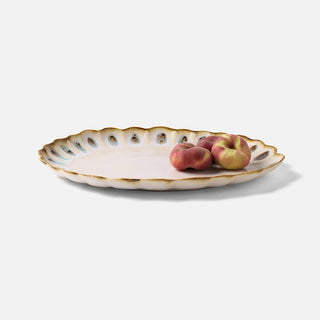 A scalloped ceramic serving platter with a gold-trimmed rim and blue-gray leaf accents along the edge, shown on a light gray background with three peaches placed on top.