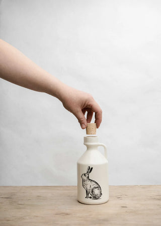 Person holding a cork on a ceramic bottle with a rabbit design against a plain background
