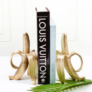 A set of two gold-finished banana bookends with a book placed between them.