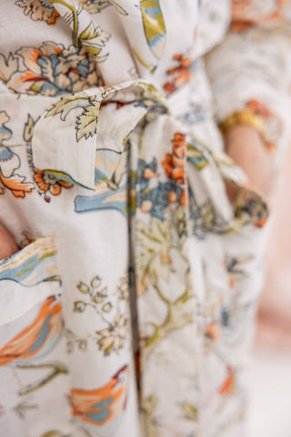 Close-up of a cream-colored cotton robe with a colorful floral and bird pattern, featuring a tie belt and a pocket.
