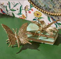 Gold butterfly and dragonfly decorative items on a green surface with a floral-patterned box in the background.