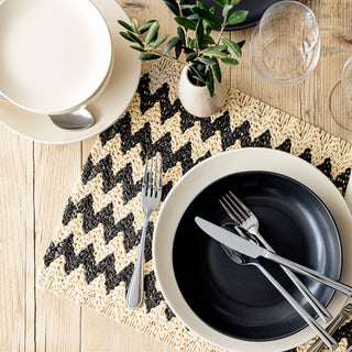 Dining table setting with black plates, silverware, and a natural chevron placemat.