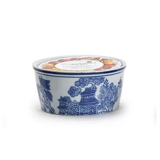 A small round ceramic tin with a blue and white traditional Chinese pagoda pattern, featuring a colorful circular label on top, set against a plain white background.