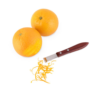 A citrus zester with an acacia handle alongside two oranges and a small pile of zest strips on a white background.