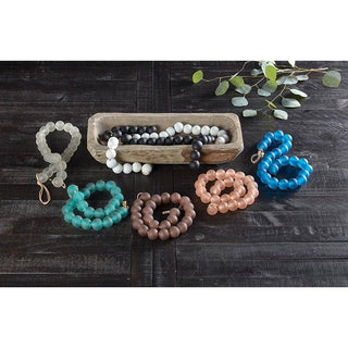 Colorful beaded garlands on a dark wooden surface with a decorative box and greenery.