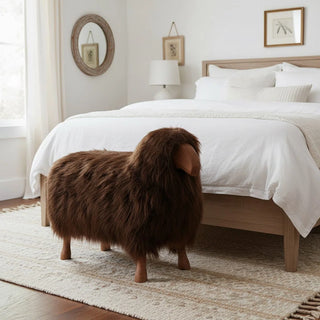 Brown fur ottoman in front of a neatly made bed in a bedroom.