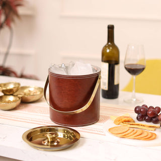 Brown leather ice bucket with gold accents on a table with wine and snacks.