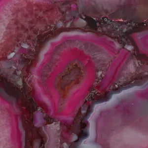 A close-up of a polished agate or jasper stone slice with concentric bands of vivid magenta pink, deeper purple, burgundy, and gray-brown crystalline patterning.