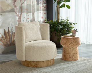 A cream bouclé accent chair with a circular natural wood base, styled in a bright room next to a sculptural cork side table.