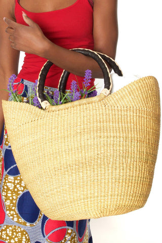 Person holding a straw bag with flowers, wearing a red top and colorful skirt.