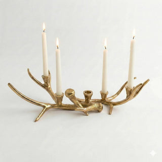 A gold-toned antler-shaped candle holder with four lit white taper candles, photographed against a clean white background.