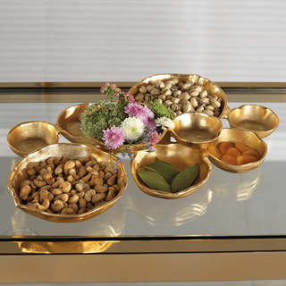A gold bowl cluster centerpiece filled with various food items like nuts and vegetables, placed on a table.