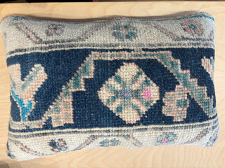 A square handwoven vintage rug pillow with a geometric pattern in navy blue, beige, light blue, and pink. Each one unique