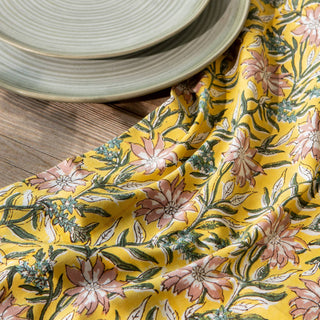 Floral-patterned yellow tablecloth on a wooden table with ceramic plates.