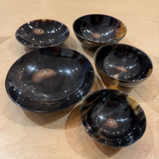 Five glossy black bowls with natural tortoiseshell patterns, arranged on a light wood surface.