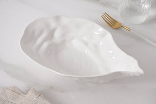 White melamine oyster shaped serving dish on a marble surface with a gold fork.