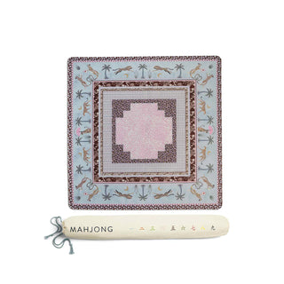 A square decorative textile or rug shown flat on a white background, with a matching rolled cream-colored storage sleeve below it. The textile has an ornate border with small illustrated motifs and a pale pink central panel.