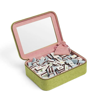 An open rectangular game box with a light olive green fabric exterior and a pink velvet interior. The box is filled with many small white and gray game pieces, and a small pink drawstring pouch sits inside.