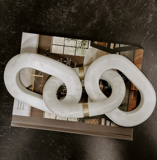 Two white marble decorative links with brass inlay placed on a magazine.