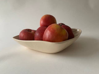 A cream-colored ceramic bowl filled with red apples, set against a plain light gray background.
