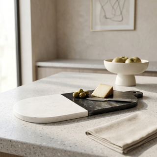 Modern kitchen setup with a marble countertop featuring a cutting board, knife, and small bowl of fruit.