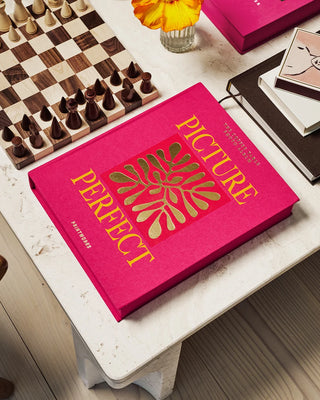 Pink album with 'Picture Perfect' text on a table with chessboard and books