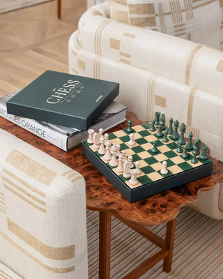 Chessboard with pieces on a wooden table next to a book titled 'Chess'.