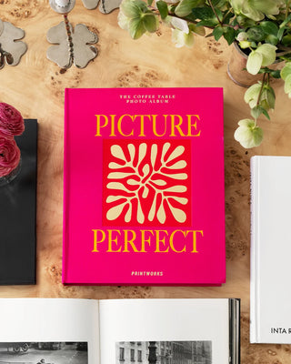 Pink book titled 'Picture Perfect' on a wooden surface with flowers and a black album.