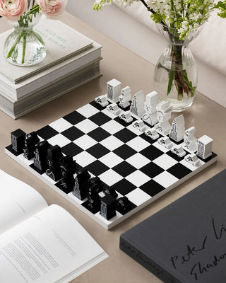 Black and white chessboard with chess pieces on a table with books and flowers.