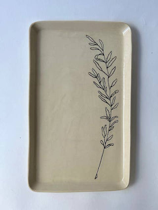 A rectangular ceramic serving tray with rounded corners in a warm beige glaze, featuring a simple black line art illustration of a leafy sprig printed vertically on the right side, set against a plain white background.