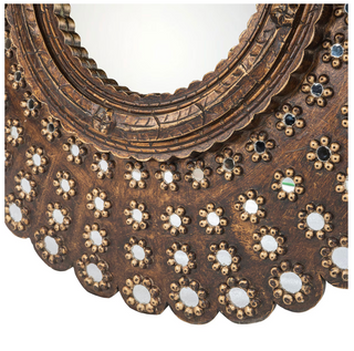 Close-up of a decorative wall mirror with an ornate scalloped frame. The frame is made of dark brown carved wood with repeated floral motifs featuring small mirrored circles and a few iridescent inlay accents, set against a plain white background.