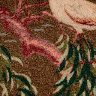 Close-up of a patterned textile or rug showing a brown base with pink branches, green leaves, and part of a cream bird.