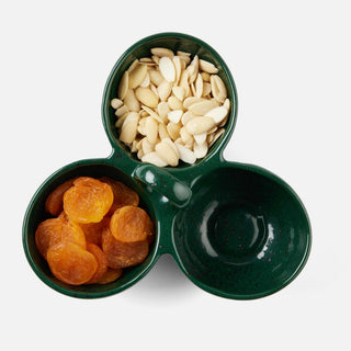 A three-compartment dark green ceramic serving bowl, shown from a top-down view on a light gray background. One compartment contains sliced almonds, another contains dried apricots, and the third is empty.