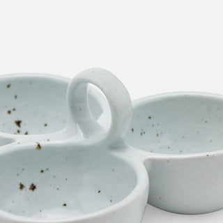 A close-up of a ceramic three-bowl serving tray with a central loop handle, featuring a pale blue-green glaze and small dark speckles, set against a clean white background.