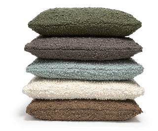 Five textured bouclé throw pillows stacked vertically on a white background, shown in olive green, charcoal gray, light blue, cream, and brown.