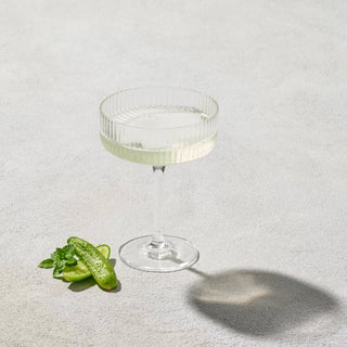Clear glass with a light green liquid on a gray surface with lime and mint leaves.